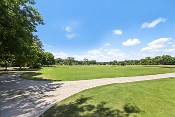 A large, open grassy area with a pathway and trees.